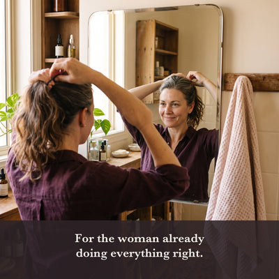A woman in her late forties putting her hair up at a bathroom mirror